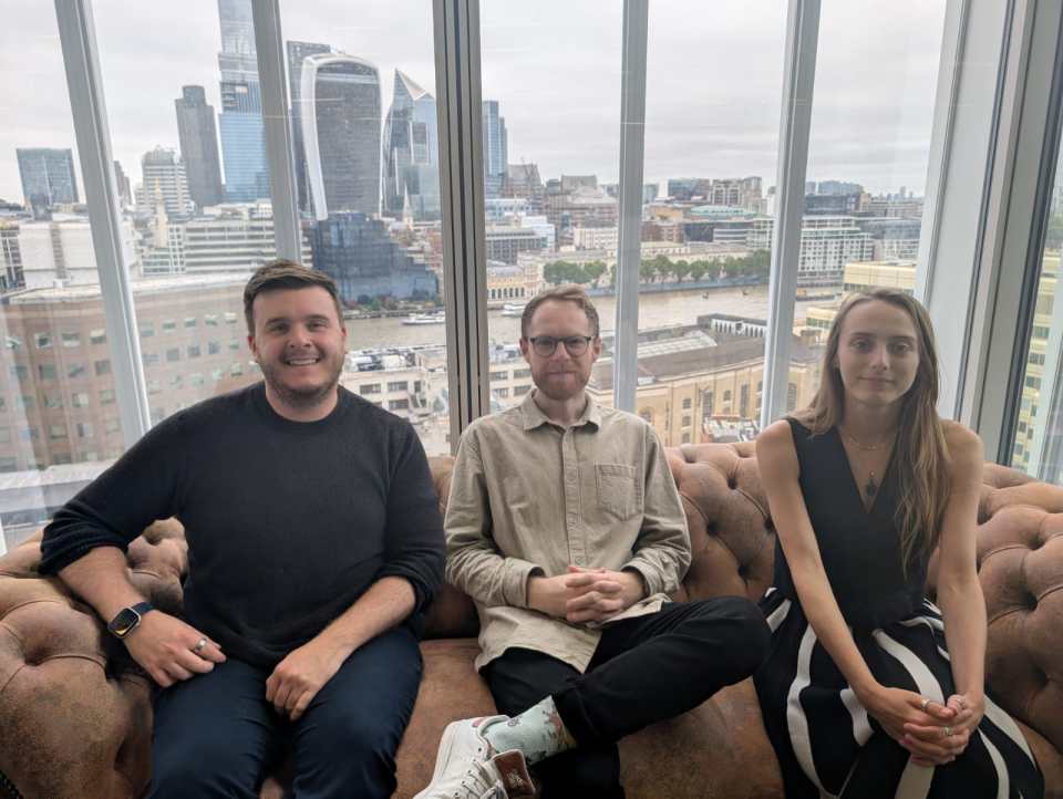 three people sit on a couch in front of a window overlooking a city