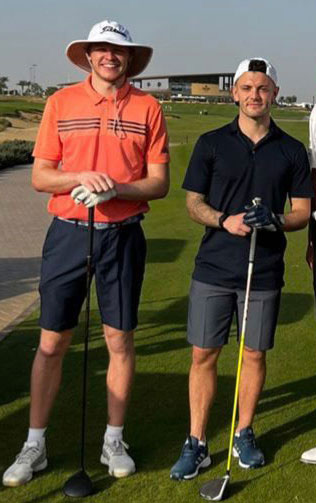 two men are standing next to each other on a golf course holding golf clubs .