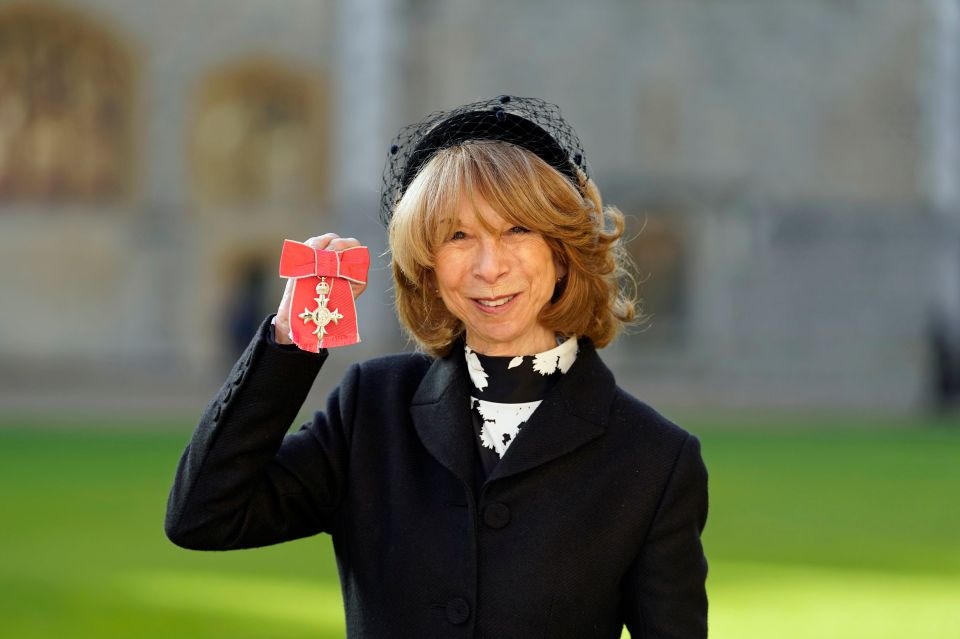 a woman in a black coat is holding a medal with a cross on it