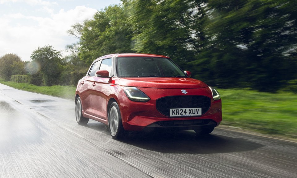 a red suzuki car is driving down a road