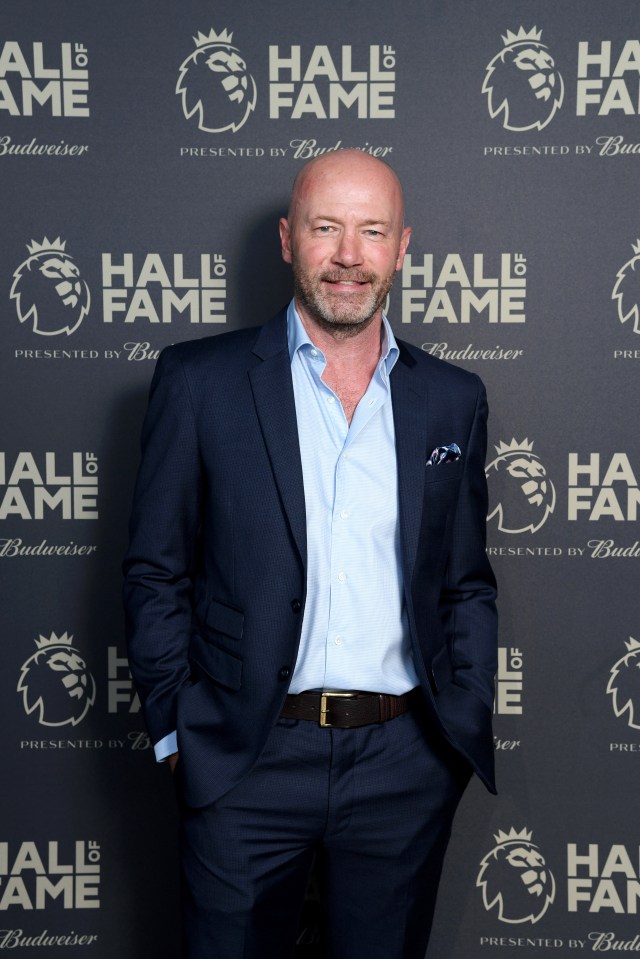 a man in a suit stands in front of a wall that says hall of fame