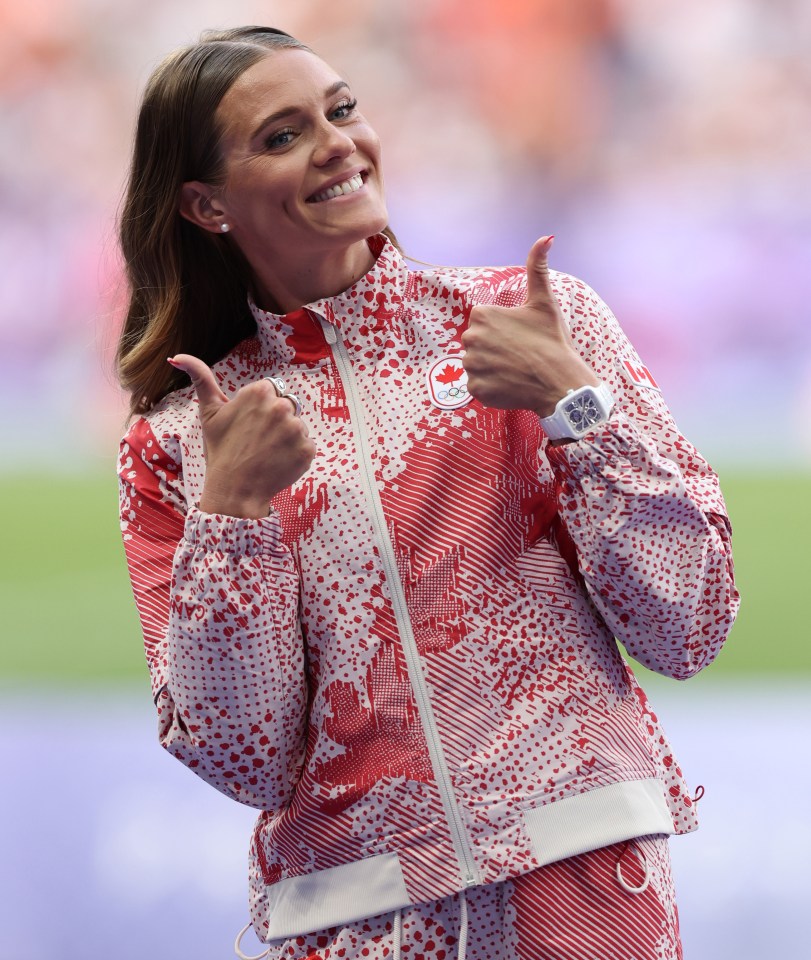 a woman wearing a jacket with a maple leaf on it gives a thumbs up