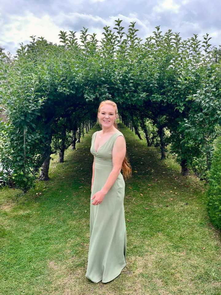 a woman in a green dress stands under an archway of apple trees