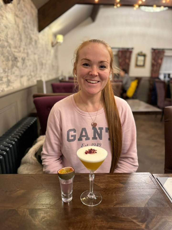 a woman wearing a gant sweatshirt sits at a table with two drinks