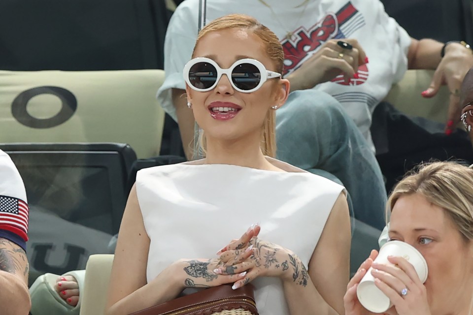 a woman wearing sunglasses sits in a stadium with other people