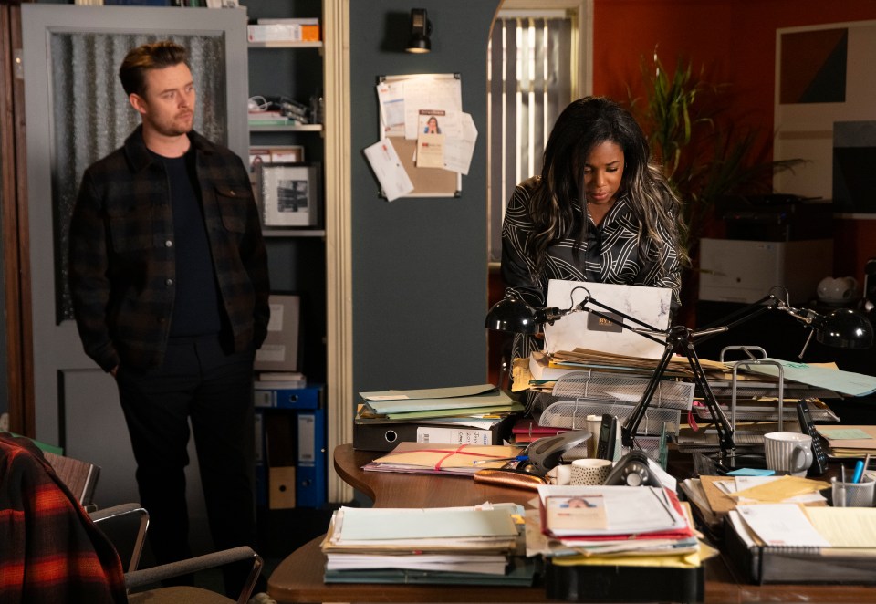 a man and a woman are standing in front of a messy desk