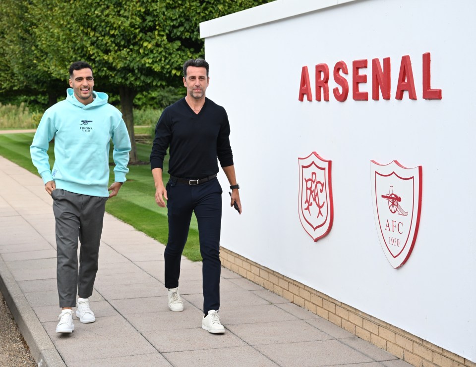 two men walking in front of a wall that says arsenal