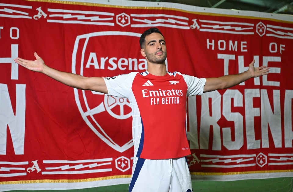 a man stands in front of a banner that says home of the arsenal