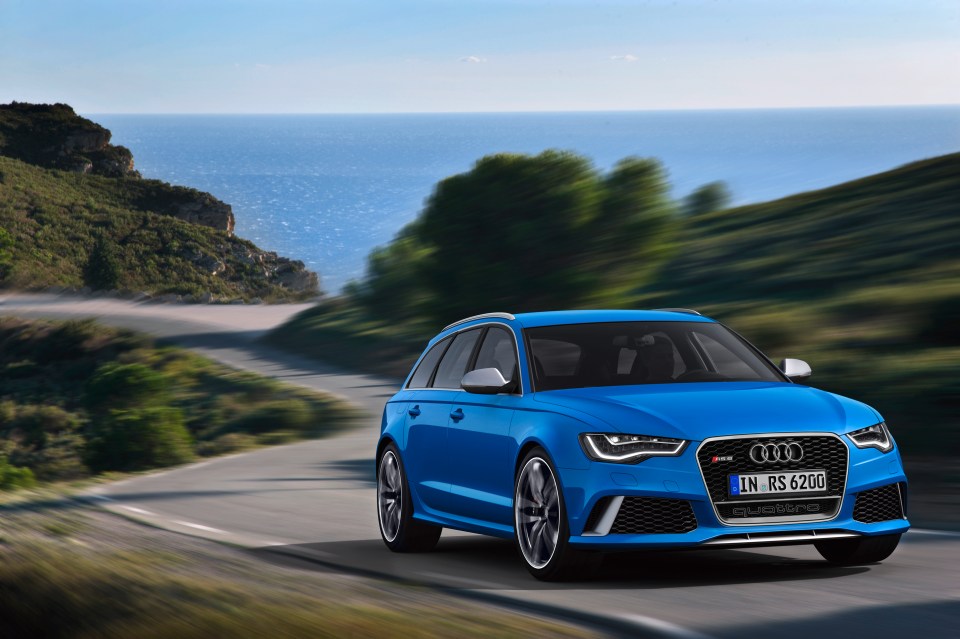 a blue audi is driving down a road near the ocean