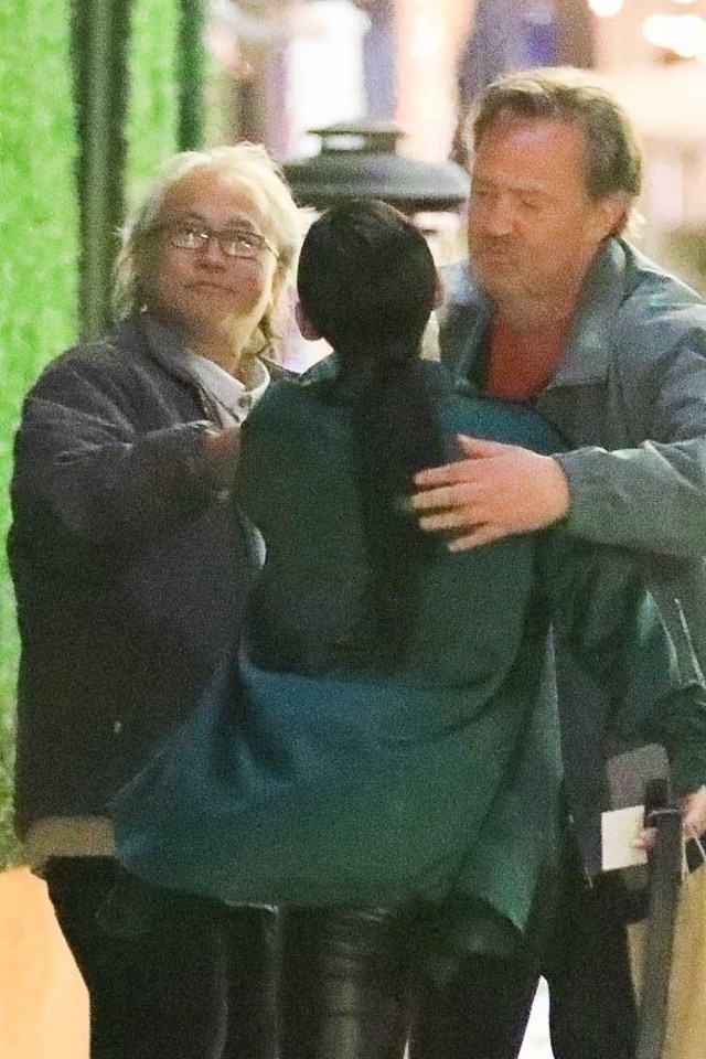 a woman in a green jacket is being hugged by two men