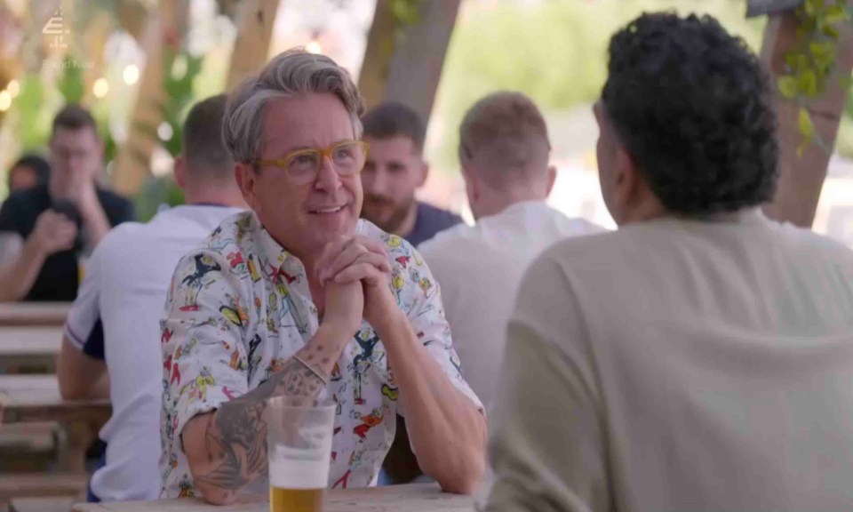 a man with glasses sits at a table with a glass of beer