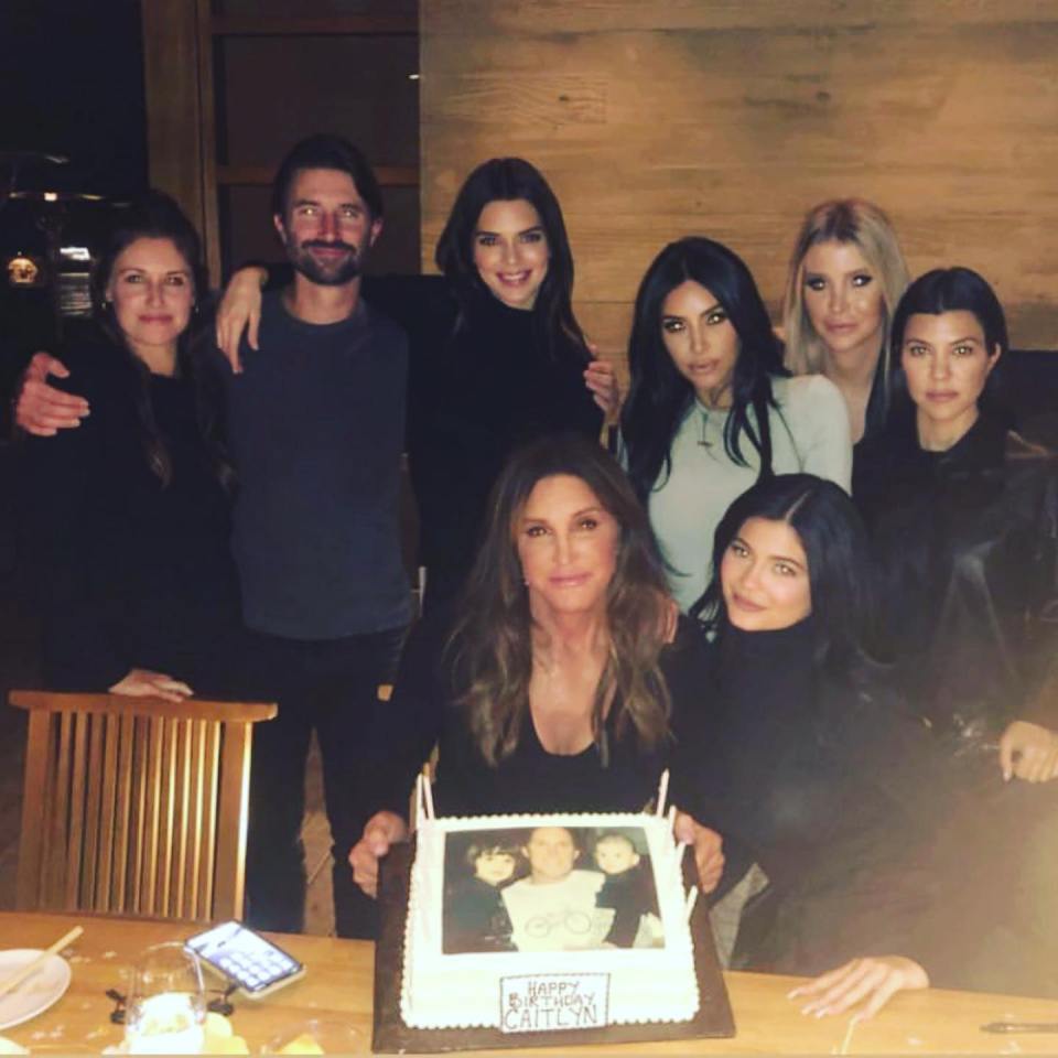 a group of people posing with a cake that says happy birthday caitlyn