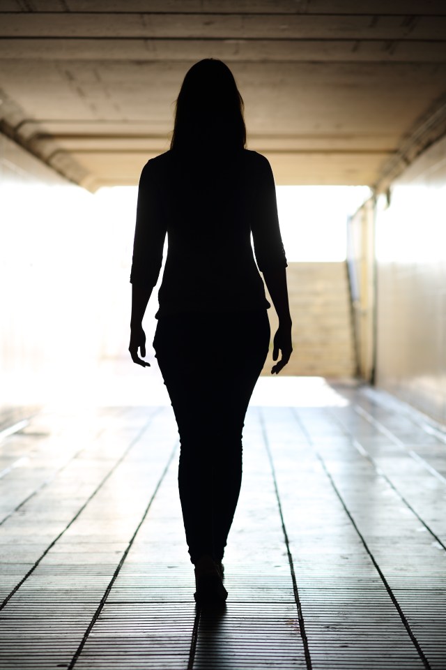 a silhouette of a woman walking through a tunnel