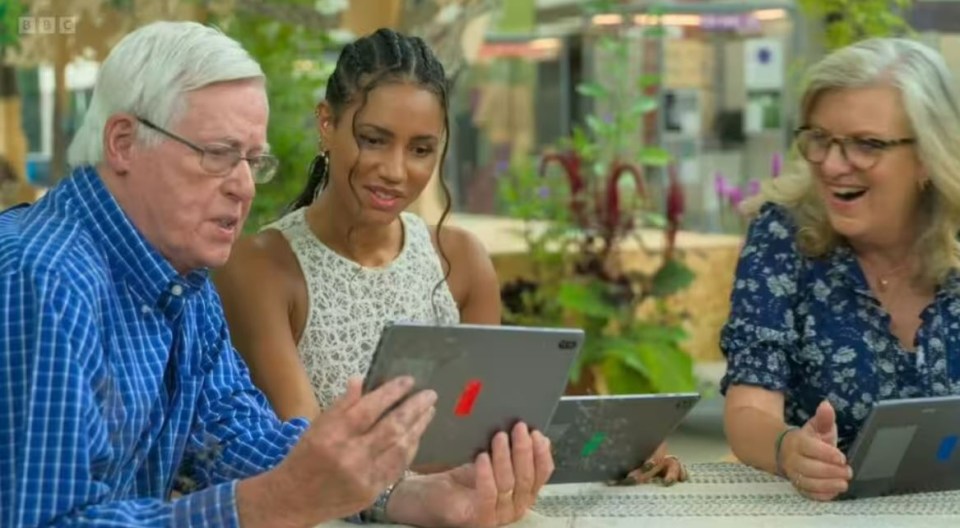 a group of people are sitting at a table looking at a tablet with the bbc logo on it