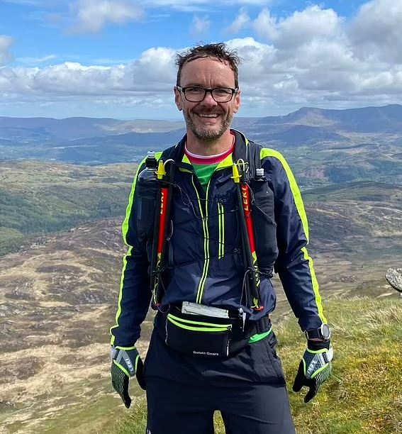 a man wearing glasses and a backpack is standing on top of a hill .