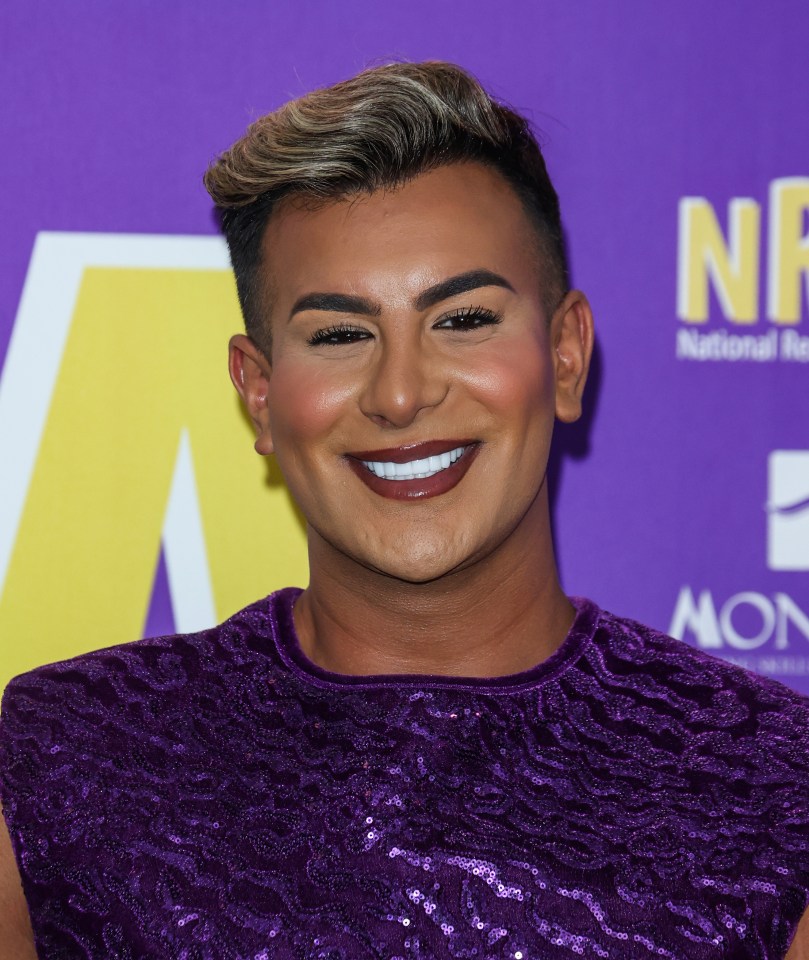 a man in a purple top smiles in front of a sign that says nr