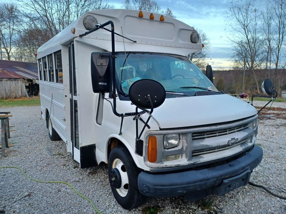 a white chevrolet bus is parked in a gravel lot