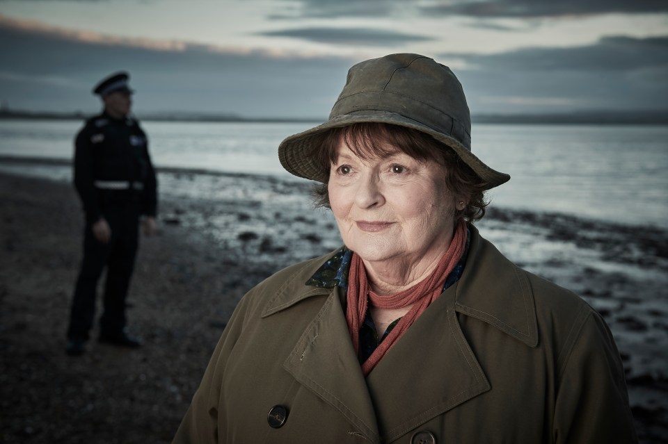 a woman in a hat stands on a beach with a police officer in the background