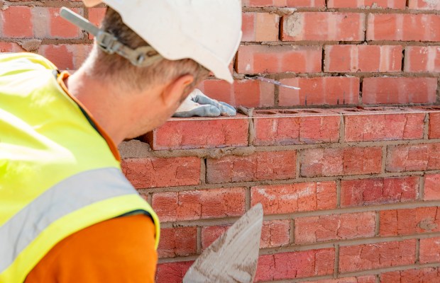 a man wearing a white hard hat is working on a brick wall