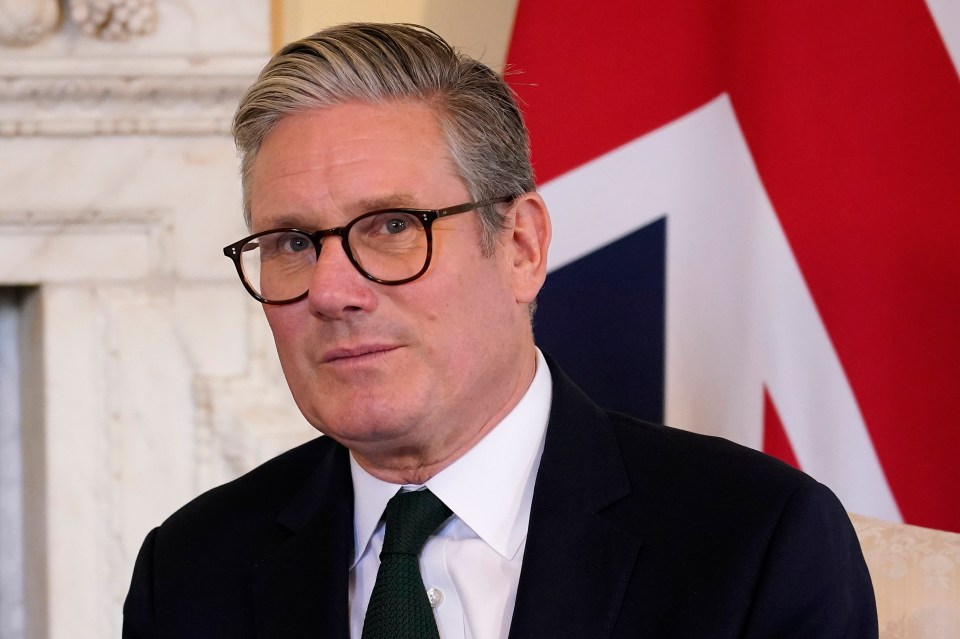 a man wearing glasses and a suit stands in front of a british flag