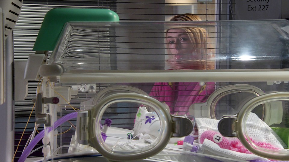 a woman looks out of an incubator with a sign that says ' security exit 227 ' on it