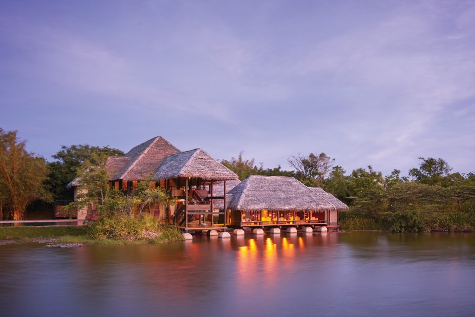 a house with thatched roofs sits in the middle of a body of water