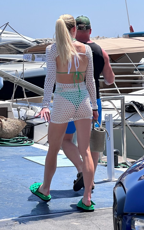 a woman in a green bikini is walking in front of a boat with the olympics logo on it