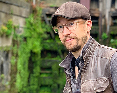 a man wearing glasses and a hat is standing in front of a building .