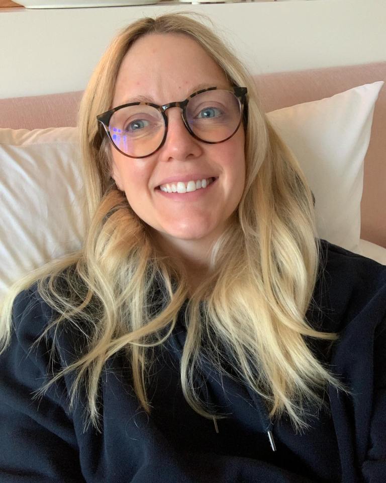 a woman wearing glasses is smiling while laying on a bed