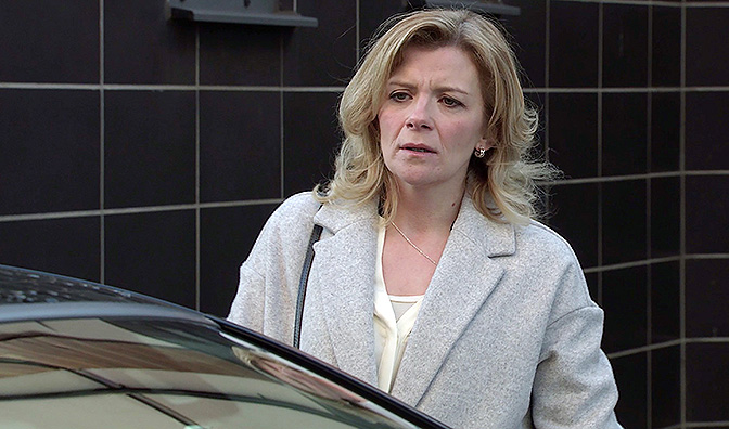 a woman in a grey coat is standing next to a car