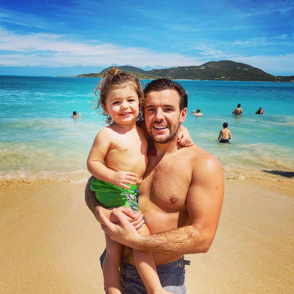 a shirtless man holds a little boy on the beach