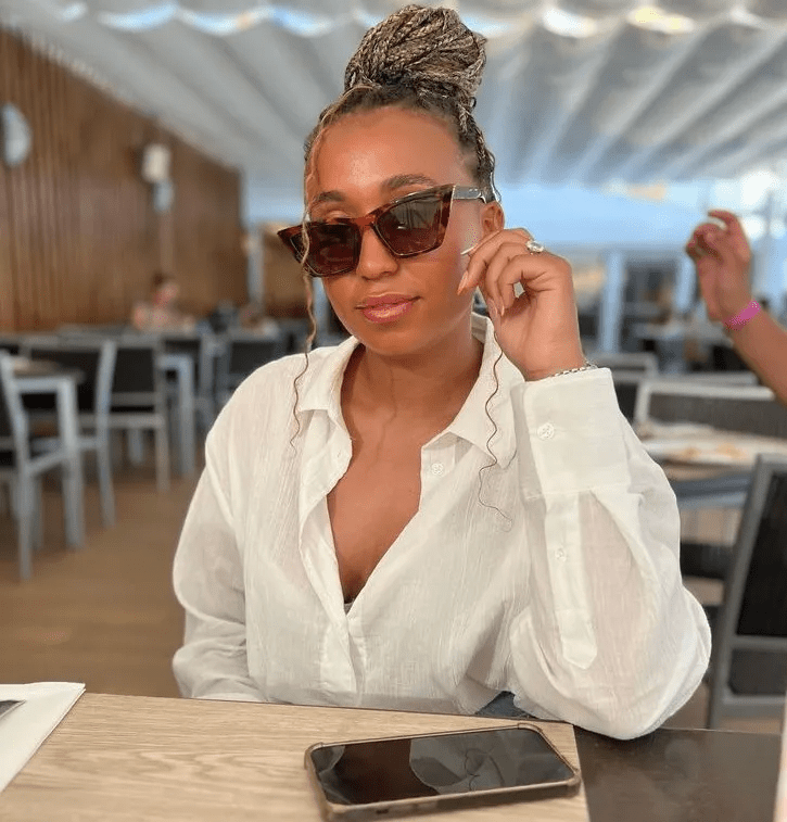 a woman wearing sunglasses and a white shirt sits at a table