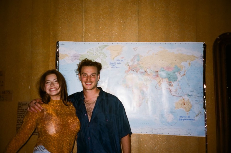 a man and a woman pose in front of a large map of the world