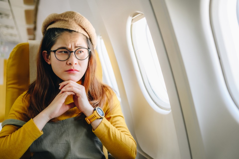 a woman wearing glasses and a watch looks out the window of an airplane