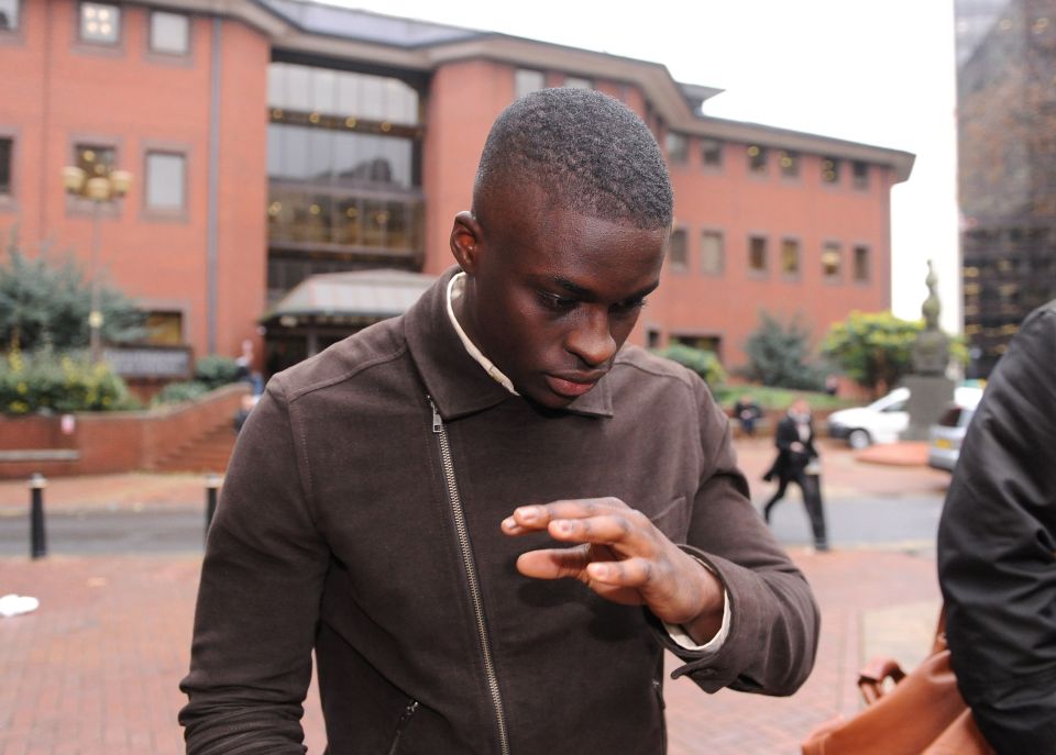 a man in a brown jacket stands in front of a brick building