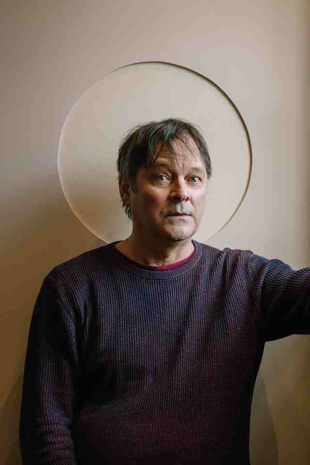 a man in a sweater stands in front of a white circle