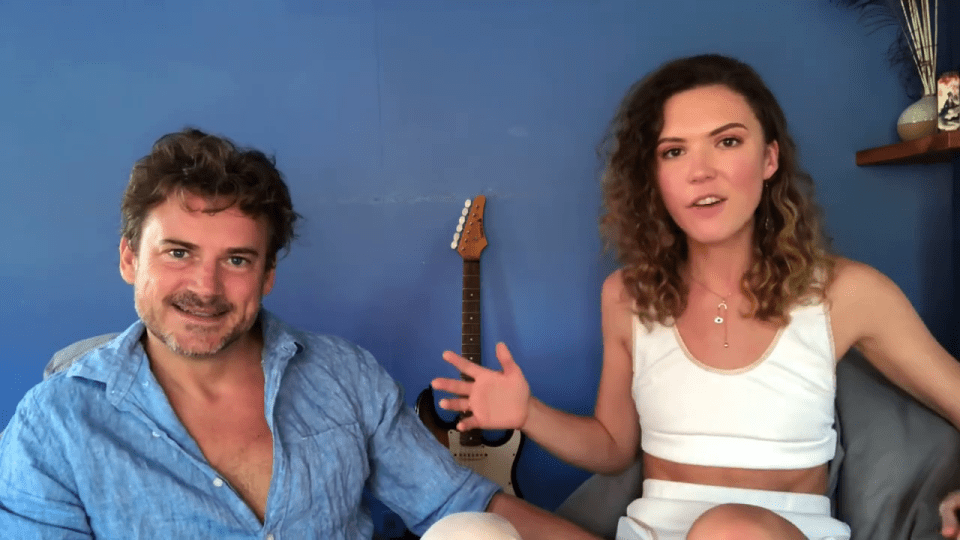 a man and a woman sitting next to each other with a guitar in the background