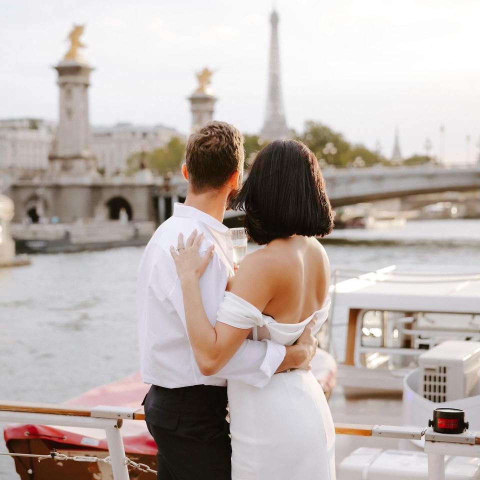 a man and a woman standing on a boat with the eiffel tower in the background