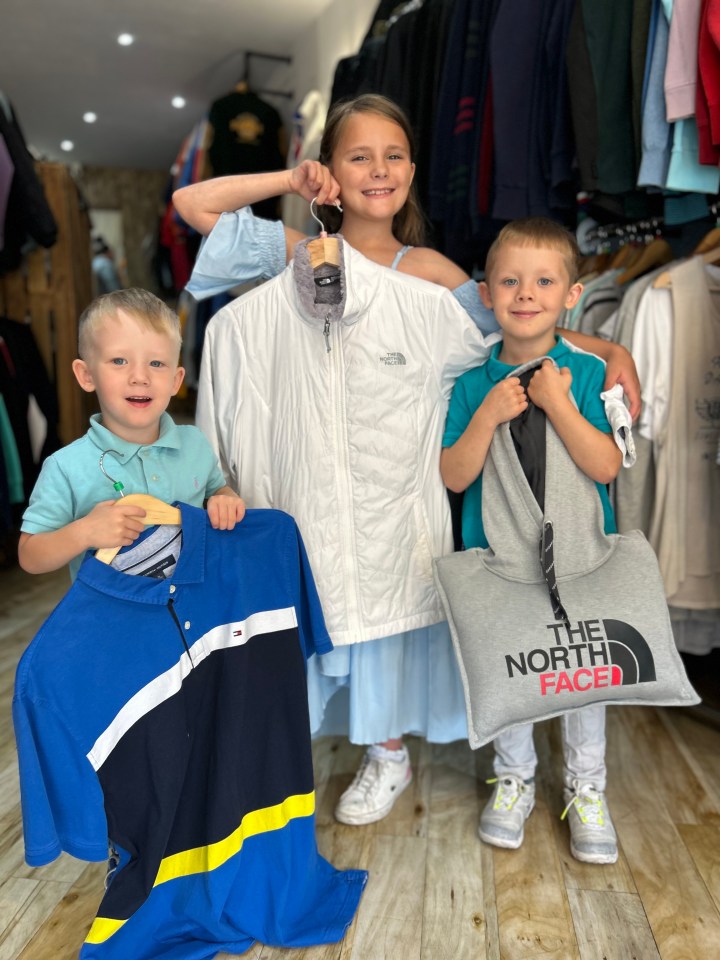 three children holding clothes and a bag that says the north face