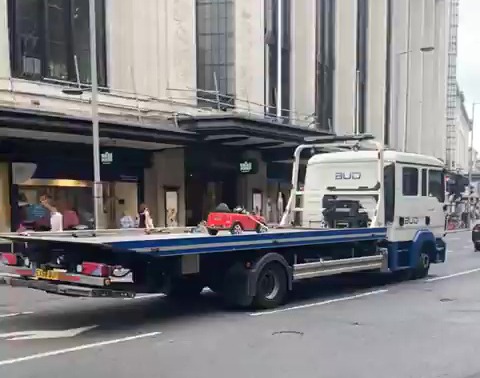 A battery powered kids’ toy car is towed away from a busy high street on the back of a flatbed lorry in London