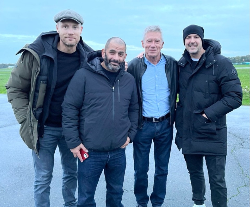 four men posing for a picture with one wearing a black jacket