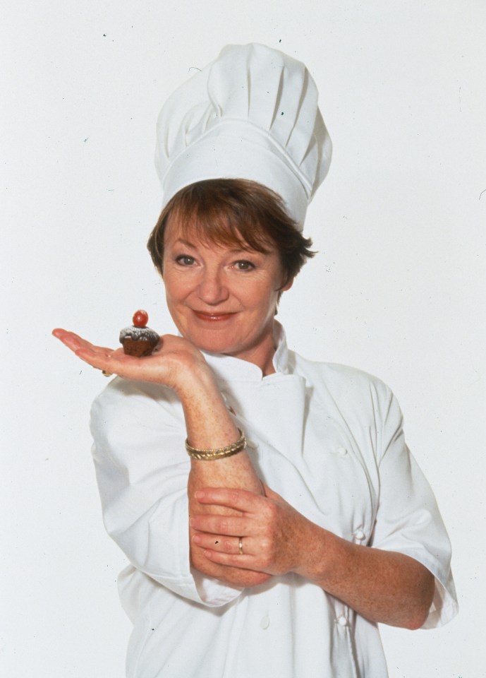 a woman in a chef 's hat is holding a cupcake in her hand