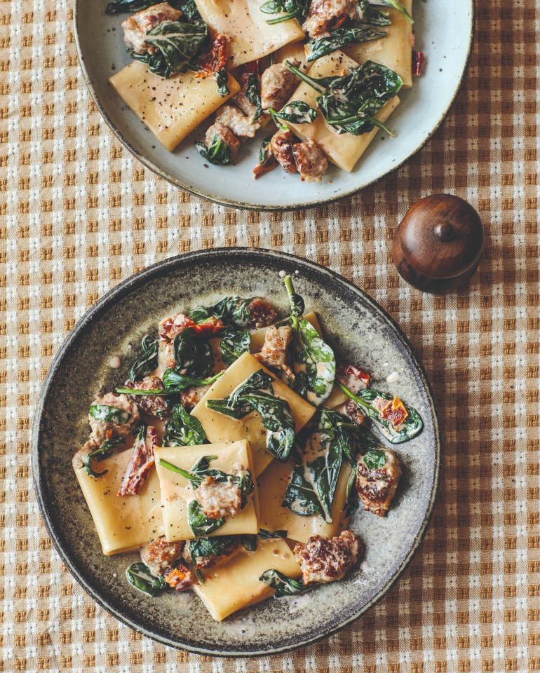 two plates of pasta with spinach and meat on a checkered table cloth