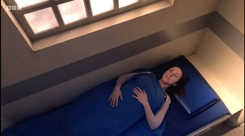 a woman wrapped in a blue blanket is laying on a bed with bbc written on the wall