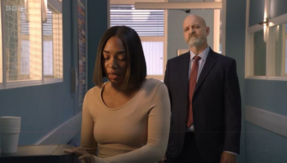 a man in a suit and tie stands next to a woman in a hallway that says bbc