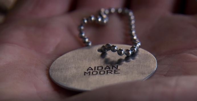 a person is holding a dog tag with the name aidan moore on it .