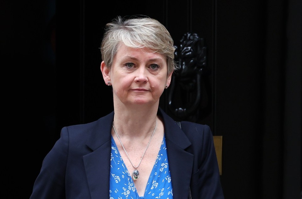 a woman wearing a blue shirt and a blue jacket stands in front of a black door