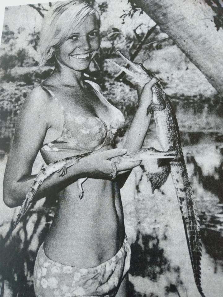 a woman in a bikini is holding a large alligator