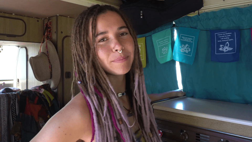 a woman with dreadlocks and a nose ring stands in front of a row of flags