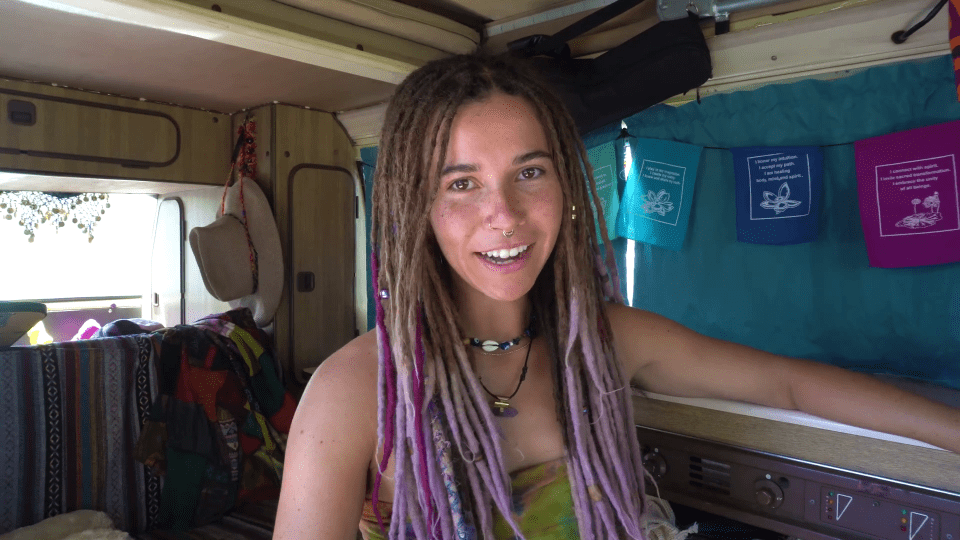 a woman with purple dreadlocks is smiling in a van